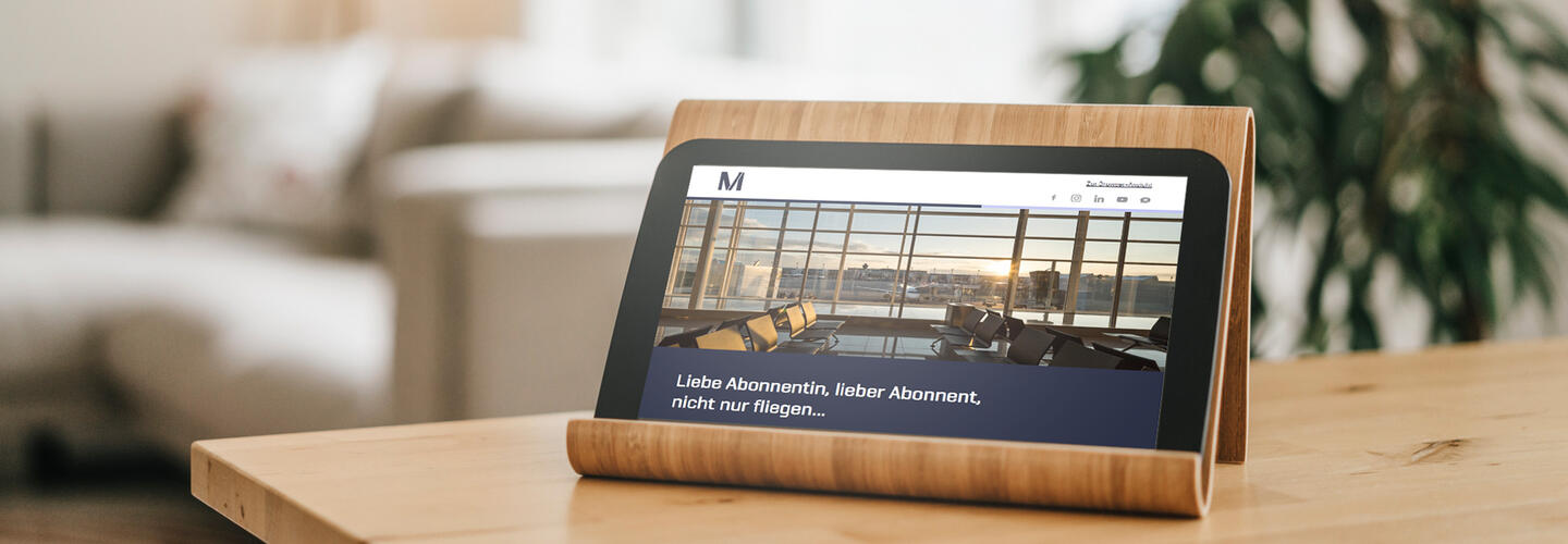 Newsletter A tablet on a wooden table displays the Munich Airport website. The modern design highlights digital services, online bookings, and customer-friendly digital offerings.