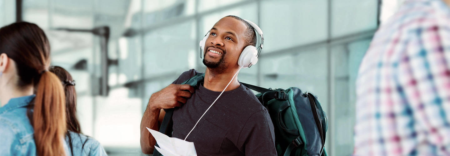 Passenger in the terminal A traveler leans back relaxed, wearing headphones and smiling while waiting for his flight in the Munich Airport terminal. The scene conveys serenity, anticipation, and relaxed travel.