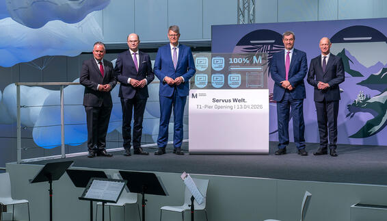 Grand Opening of Terminal 1 Pier at Munich Airport Five men are standing next to an OLED display that shows 100% and has opened the pier